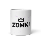 Taza ZOMKI Crew blanca: vista frontal del logotipo negro y corona sobre confeti lila
