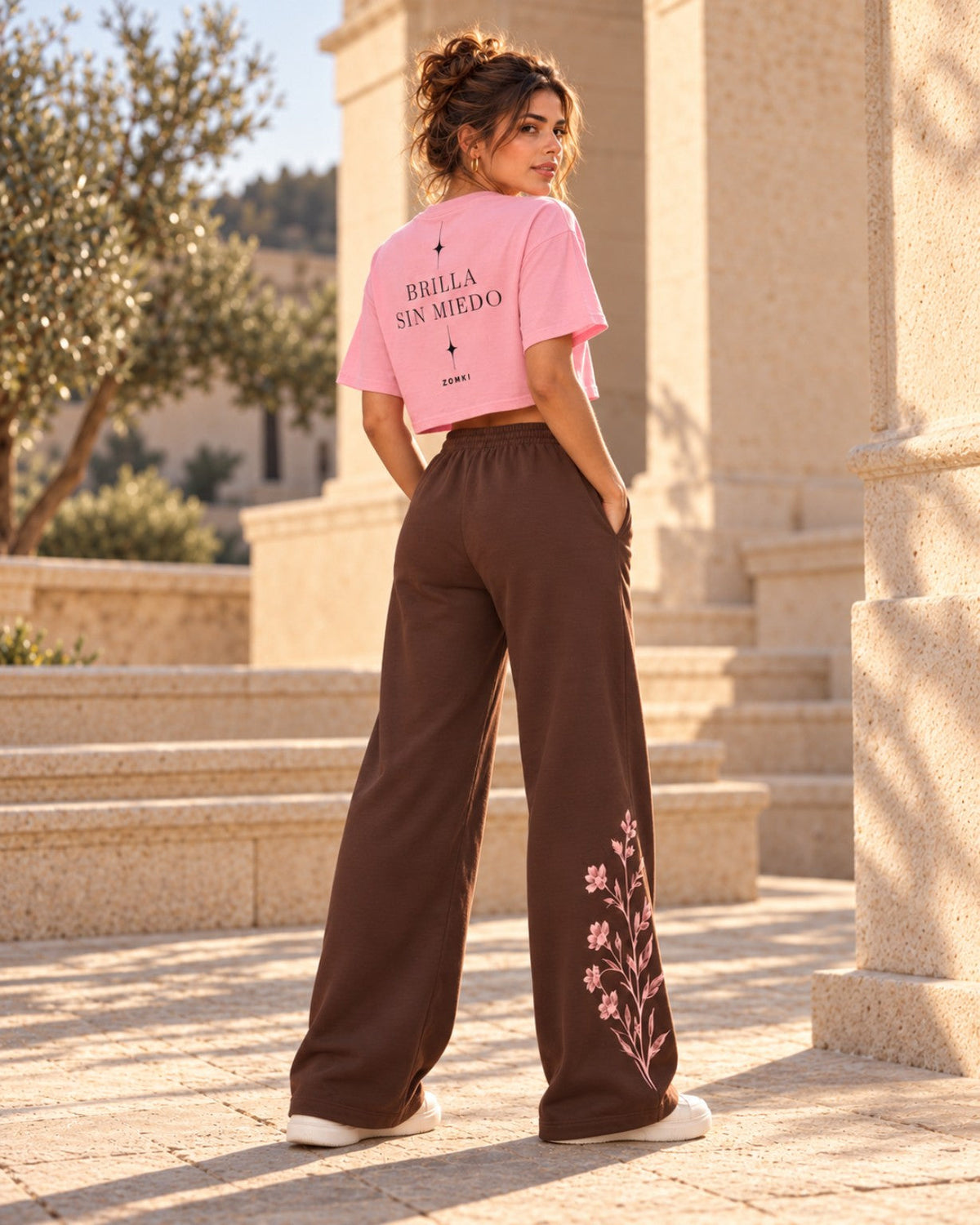 Vista trasera de estilismo con IA: camiseta corta ZOMKI rosa, texto BRILLA SIN MIEDO en la espalda y pantalón floral Soft Rebel, no incluido en esta ficha.