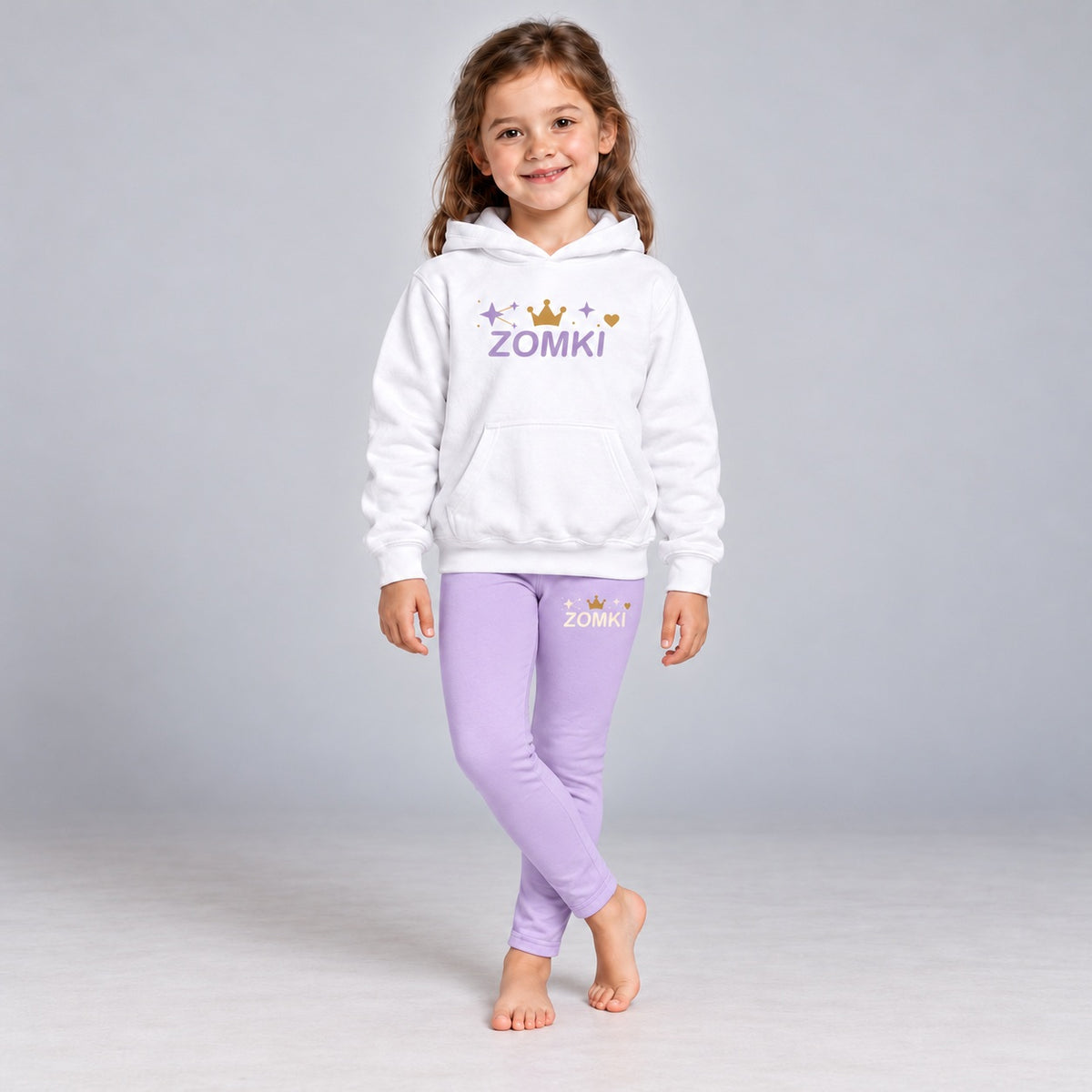 Visualización editorial generada con IA con el mismo modelo infantil sintético del conjunto ZOMKI Corona Lavanda, en una pose nueva con piernas cruzadas. Sudadera blanca y leggings lavanda con constelación de estrellas. No representa a una persona real.