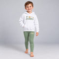 Visualización editorial generada con IA con el mismo modelo infantil sintético del conjunto ZOMKI Corona Verde salvia, en una pose nueva de paso frontal. Sudadera blanca y leggings coordinados con rayo y trazos de energía. No representa a una persona real.