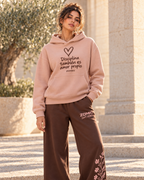 Idea de combinación: modelo con sudadera ZOMKI Disciplina también es amor propio rosa y pantalón Soft Rebel chocolate con flores. Cada prenda se vende por separado. Imagen generada con IA.