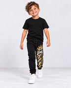 Modelo sintético generado con IA: jogger negro ZOMKI Graffiti Dorado, estampado vertical en la pierna izquierda; camiseta de estilismo no incluida