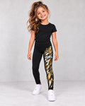 Leggings infantiles negros ZOMKI Graffiti Dorado con modelo sintético IA niña; estampado blanco y dorado con corona y corazón sobre la i en la pierna izquierda