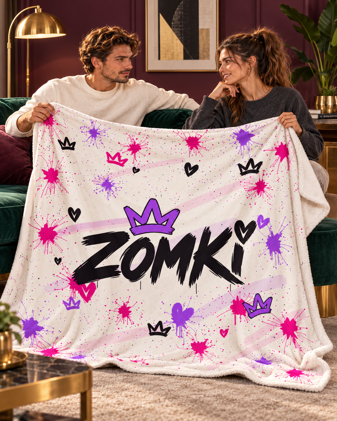 Pareja de modelos oficiales ZOMKI mirándose en salón art déco verde y ciruela con manta sherpa Purple Pink Blanco desplegada.
