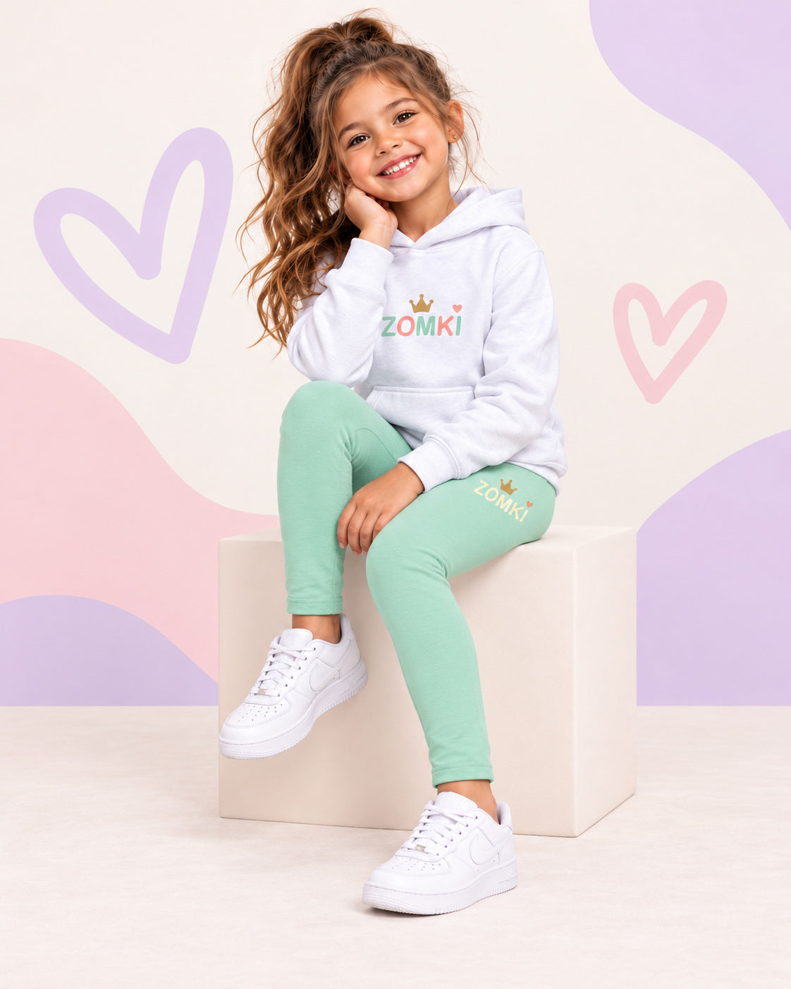 Conjunto infantil ZOMKI Corona · Menta y melocotón · Sudadera + leggings, en modelo femenina oficial ZOMKI. Se vende el conjunto de dos prendas. Imagen creada con IA; maquetas de producto en galería.