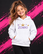 Sudadera infantil ZOMKI Corona · Blanca y lavanda, en modelo femenina oficial ZOMKI. Se vende únicamente esta prenda. Imagen creada con IA; maquetas de producto en galería.