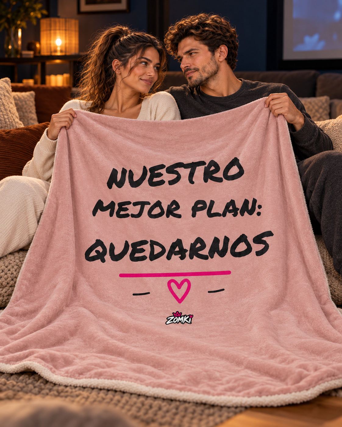 Manta sherpa ZOMKI Refugio «Nuestro mejor plan: quedarnos», con pareja ZOMKI en una sesión de cine en casa. Se vende únicamente la manta de 127 × 153 cm. Imagen de ambientación creada con IA; maquetas del producto en la galería.
